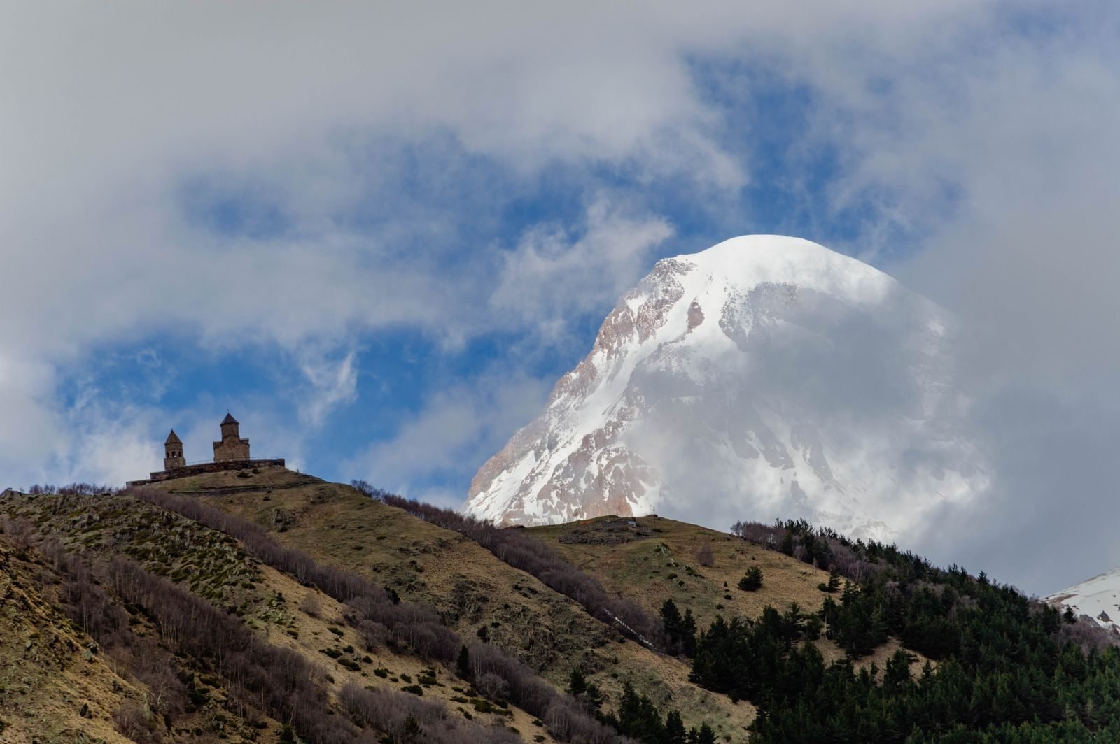 Gergeti Trinity Church standing alone on a green hilltop below the snow-capped peak of Mount Kazbek, Georgia