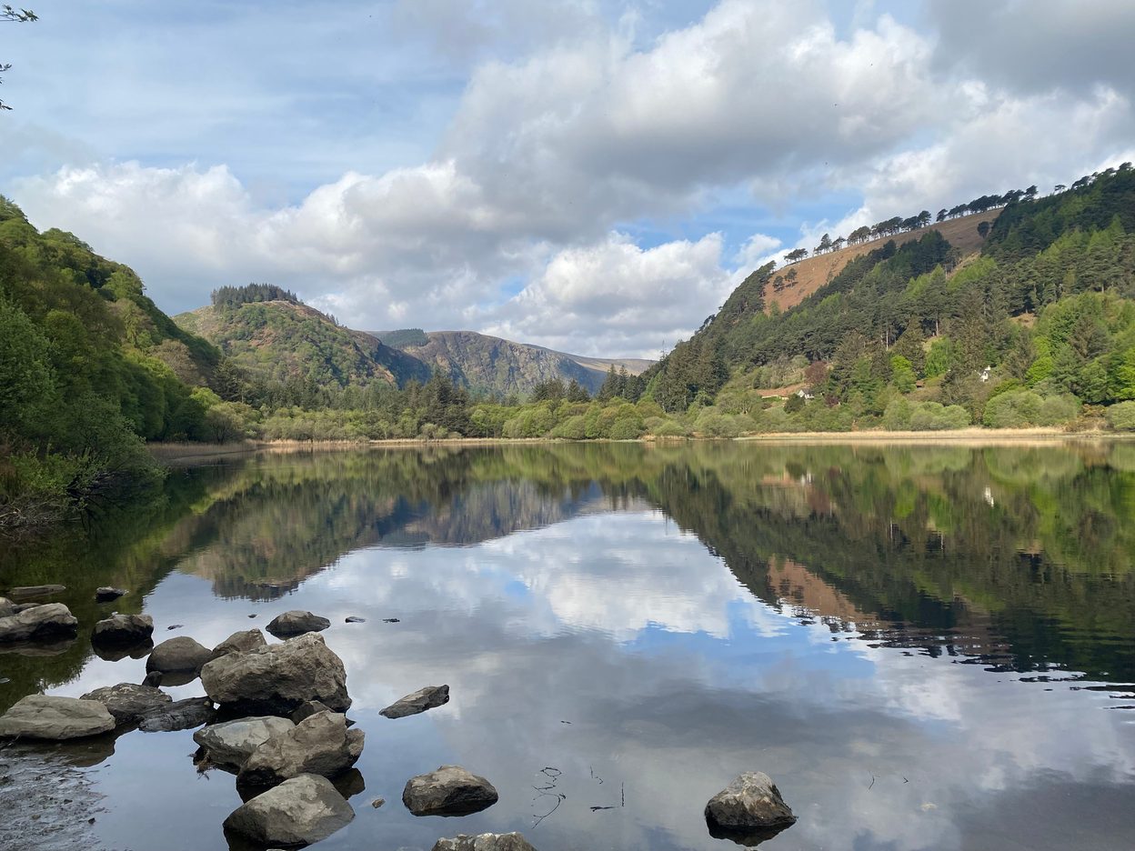 The Upper Lake at Glendalough, still and reflecting the wooded mountainsides and clouds