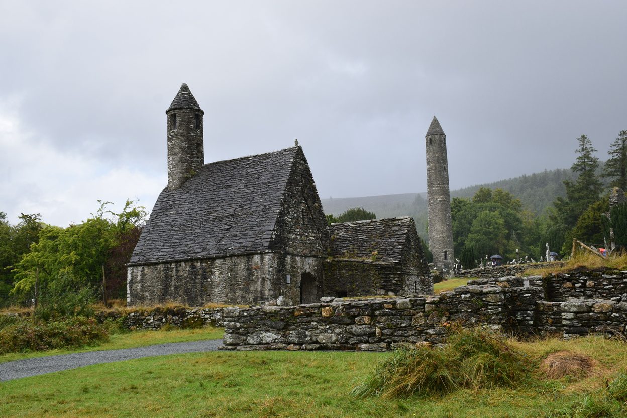 The stone-roofed St Kevin's Church and the round tower of Glendalough among green fields and trees