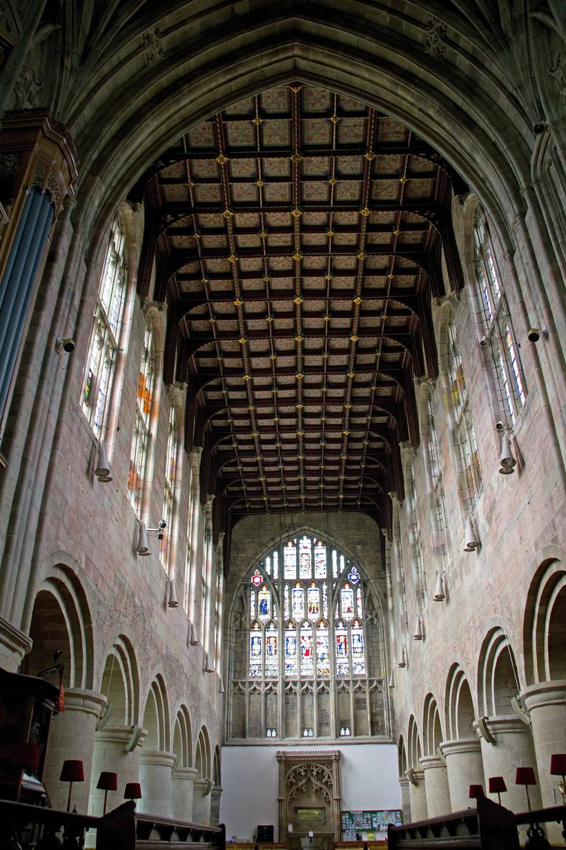 The nave of Great Malvern Priory looking east, with a timber roof and the great east window