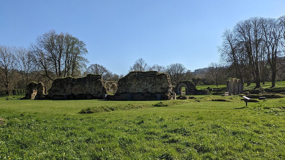 The ruins of Hailes Abbey across a wide green lawn, with bare trees and the Cotswold edge behind