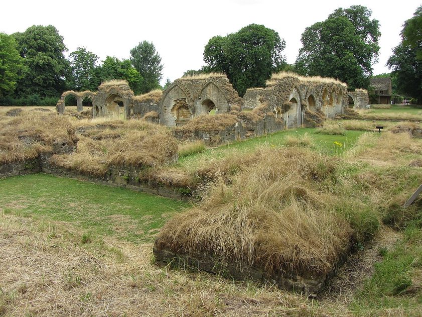 Low ruined walls of Hailes Abbey in long summer grass, with broken arches beyond and trees behind