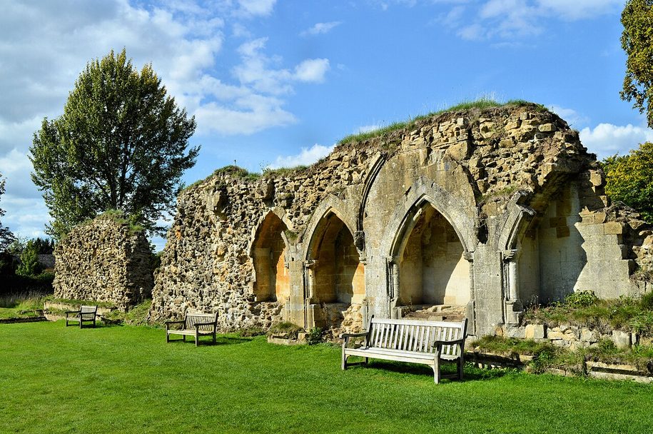 The ruined arches on the east side of the cloister at Hailes Abbey, Gloucestershire, with a bench on the lawn in front