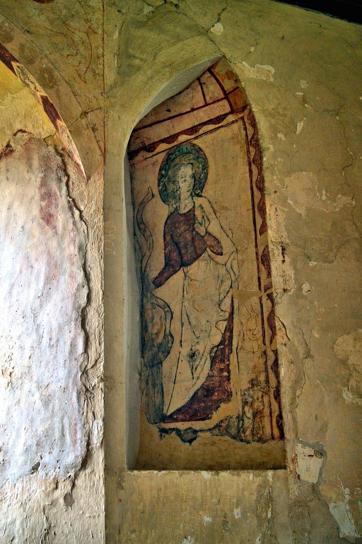 A faded medieval wall painting of a saint in a pointed recess on the wall of Hailes church