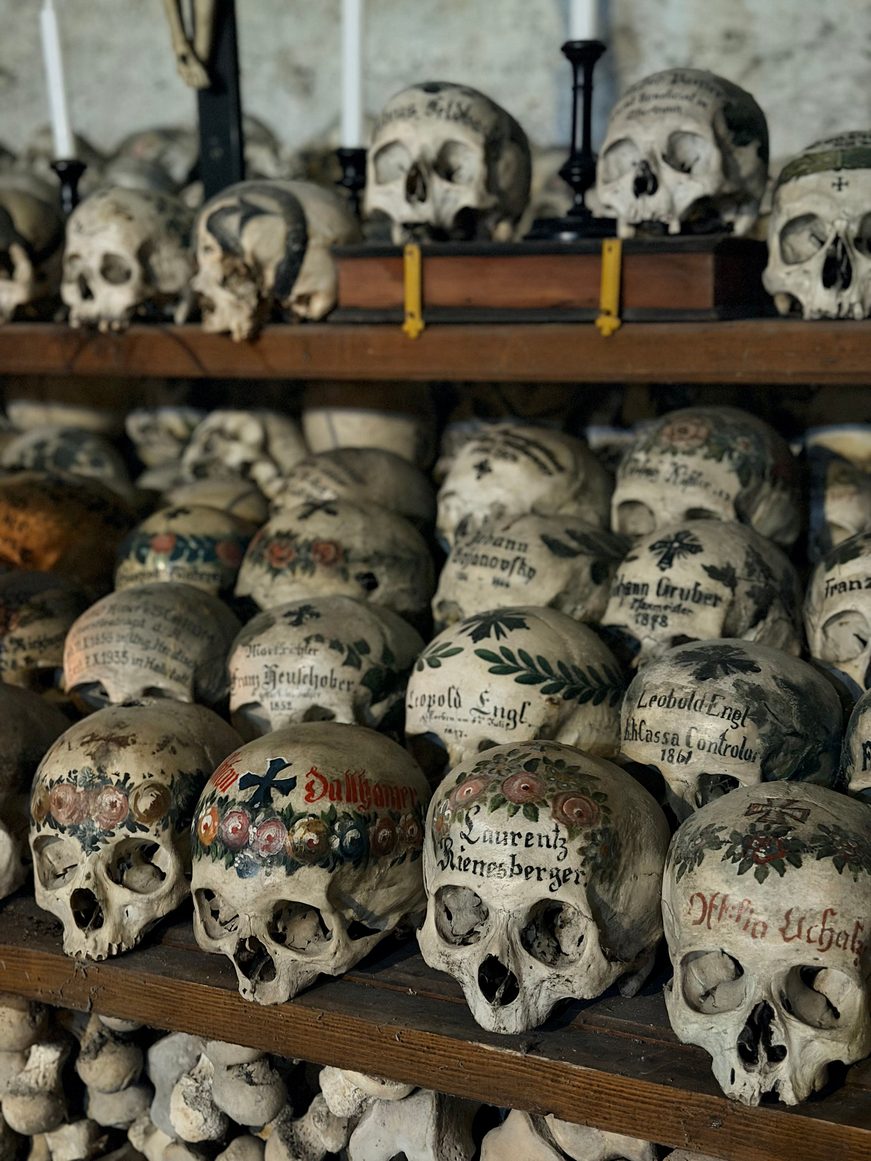 Rows of painted skulls on wooden shelves above stacked bones in the Hallstatt charnel house
