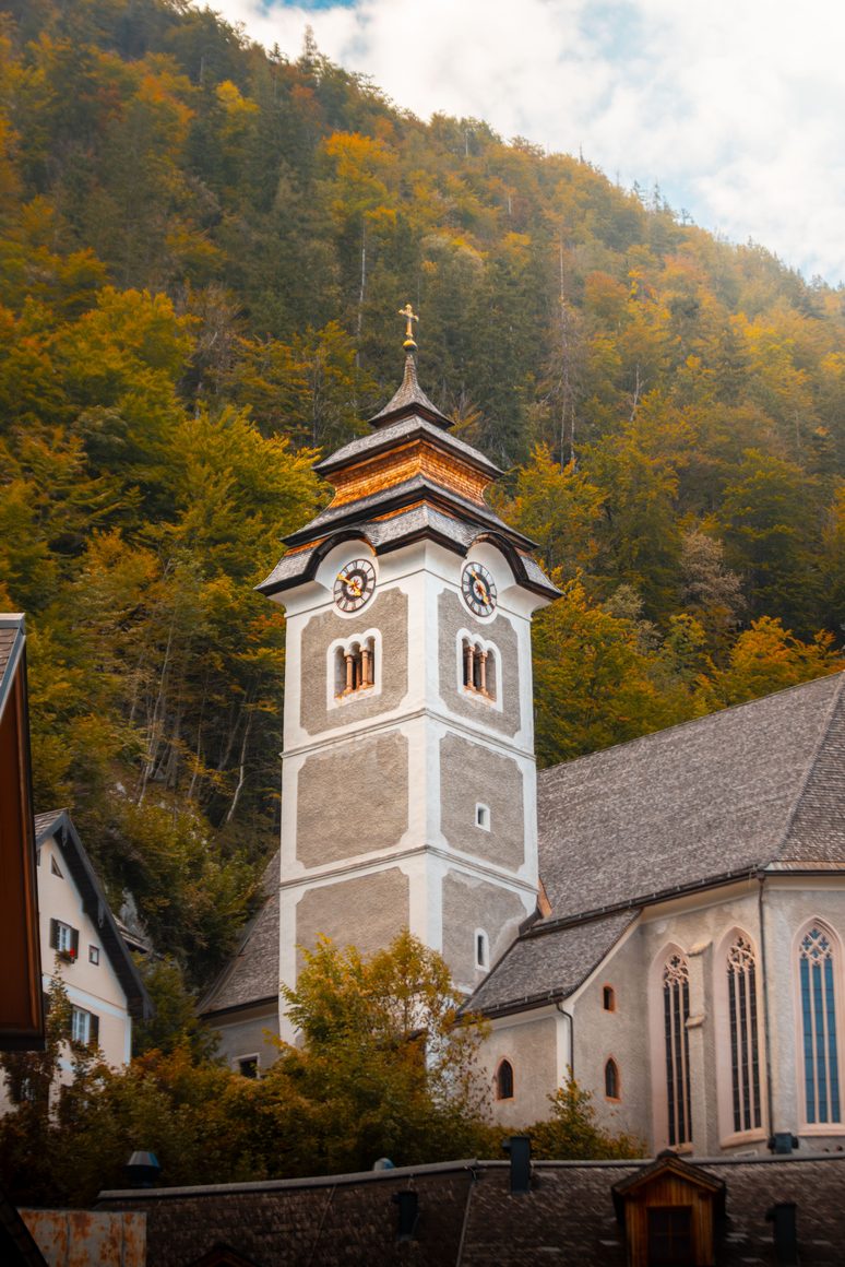 The white tower of the Catholic parish church of Hallstatt among autumn trees