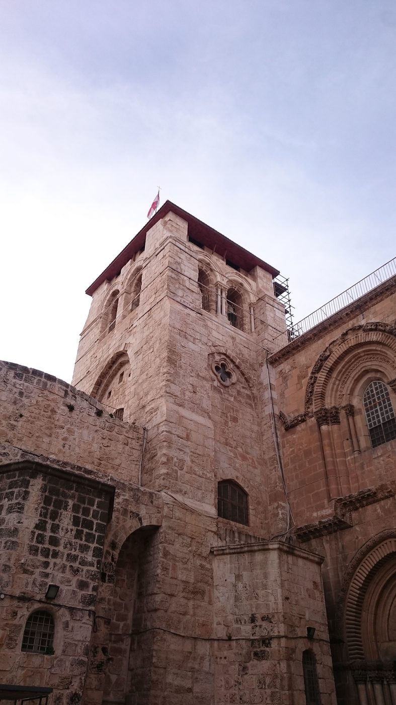The squat stone bell tower of the Church of the Holy Sepulchre against a pale sky