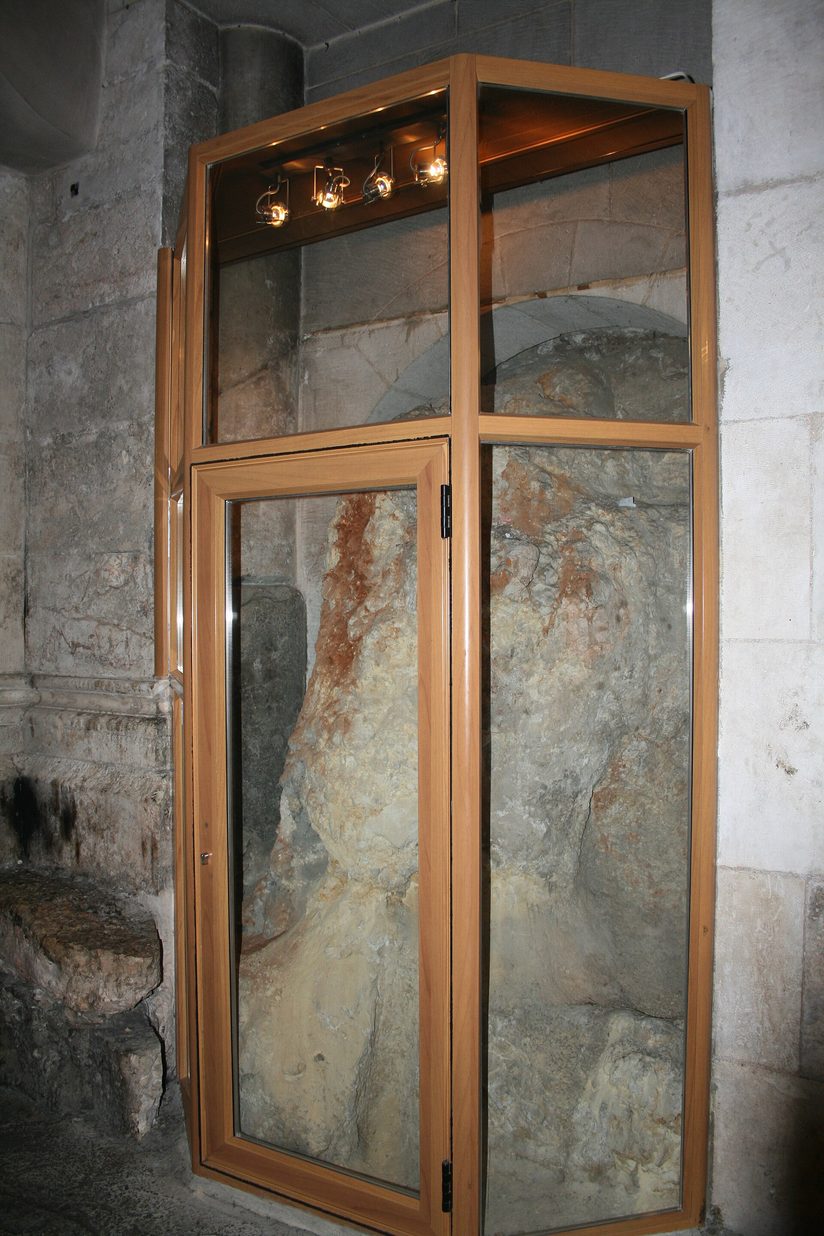 The bare rock of Calvary seen through a glass case set into a stone wall in the Church of the Holy Sepulchre