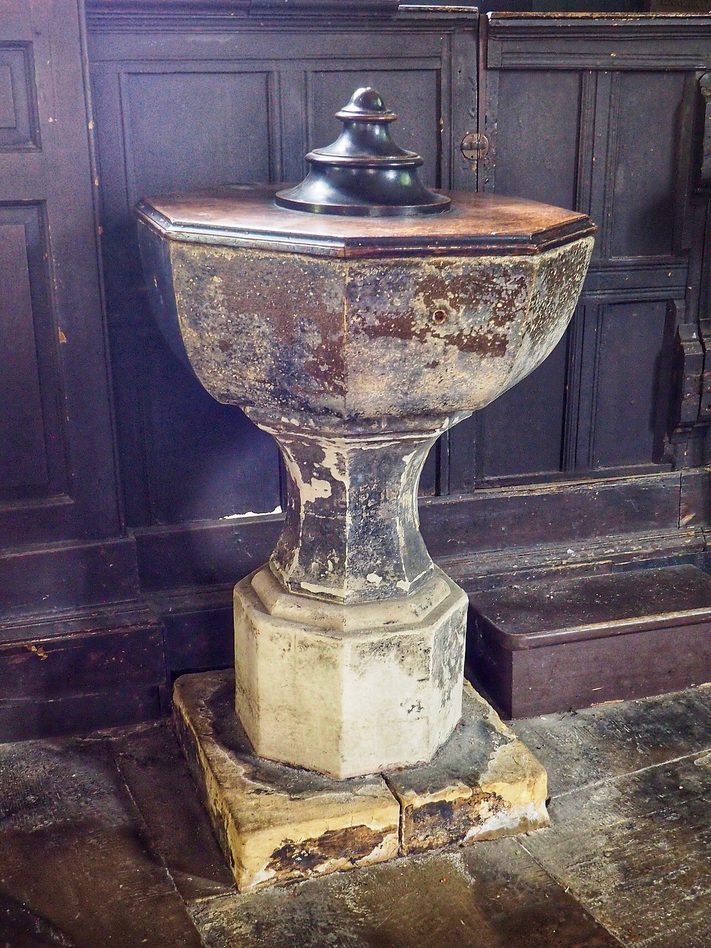 A simple stone font with a dark wooden cover in Holy Trinity Church, Goodramgate, York