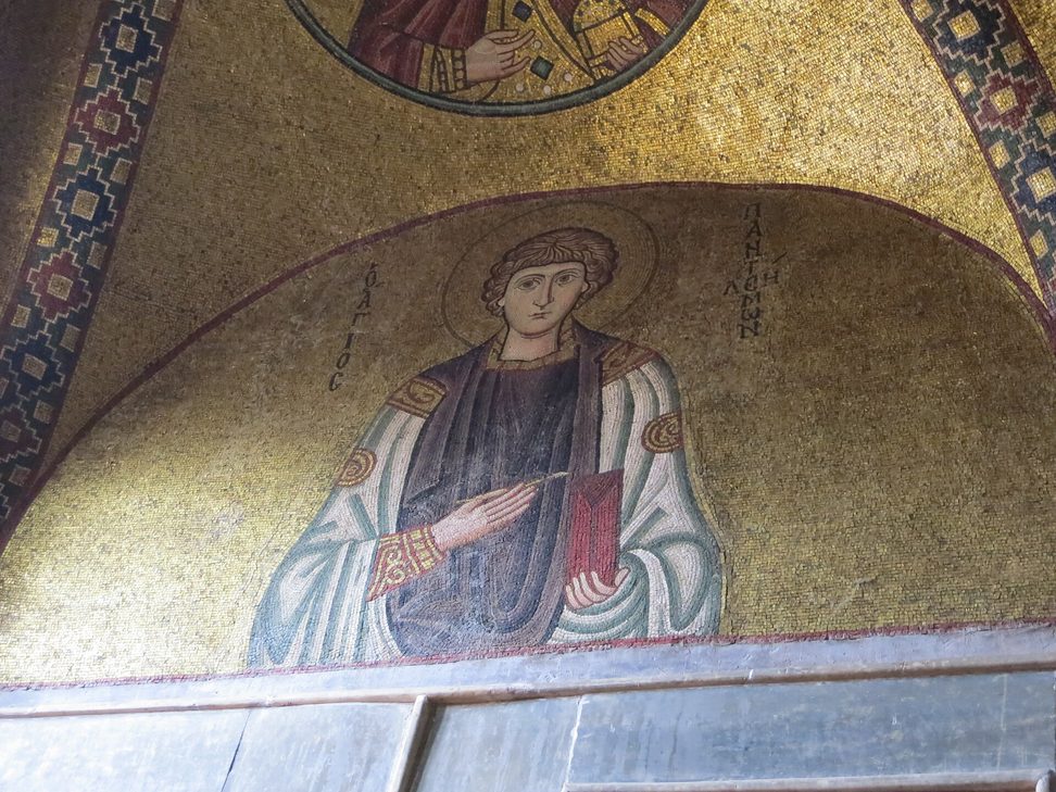 A mosaic of a young saint in a richly patterned robe on a gold ground, in a lunette at Hosios Loukas
