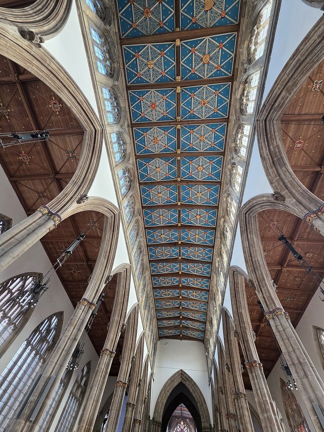 Looking up at the painted blue and gold roof of the nave at Hull Minster between tall arches