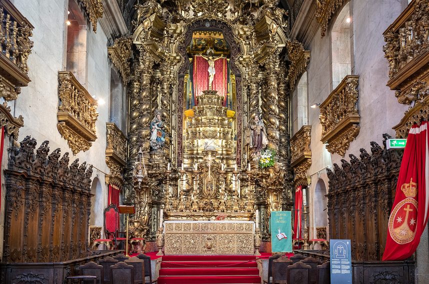 The gilded high altarpiece of the Igreja do Carmo above red carpeted steps, with carved wooden choir stalls on either side