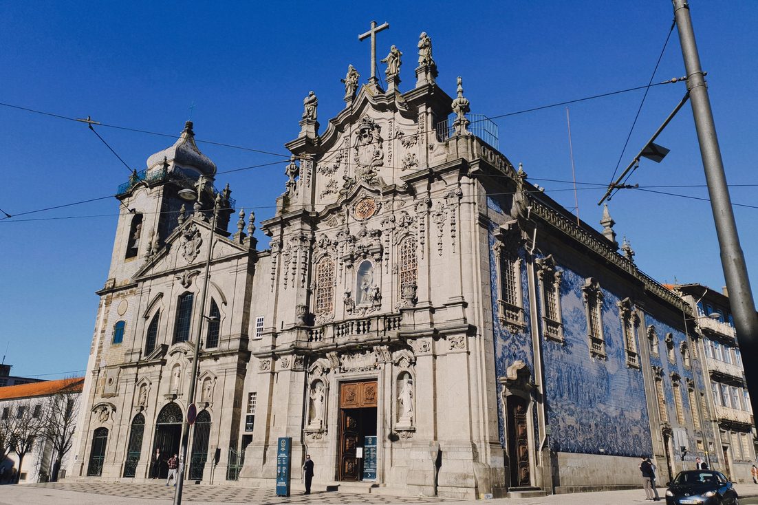 The ornate grey stone Rococo facade of the Igreja do Carmo in Porto, with its long side wall covered in blue and white tiles
