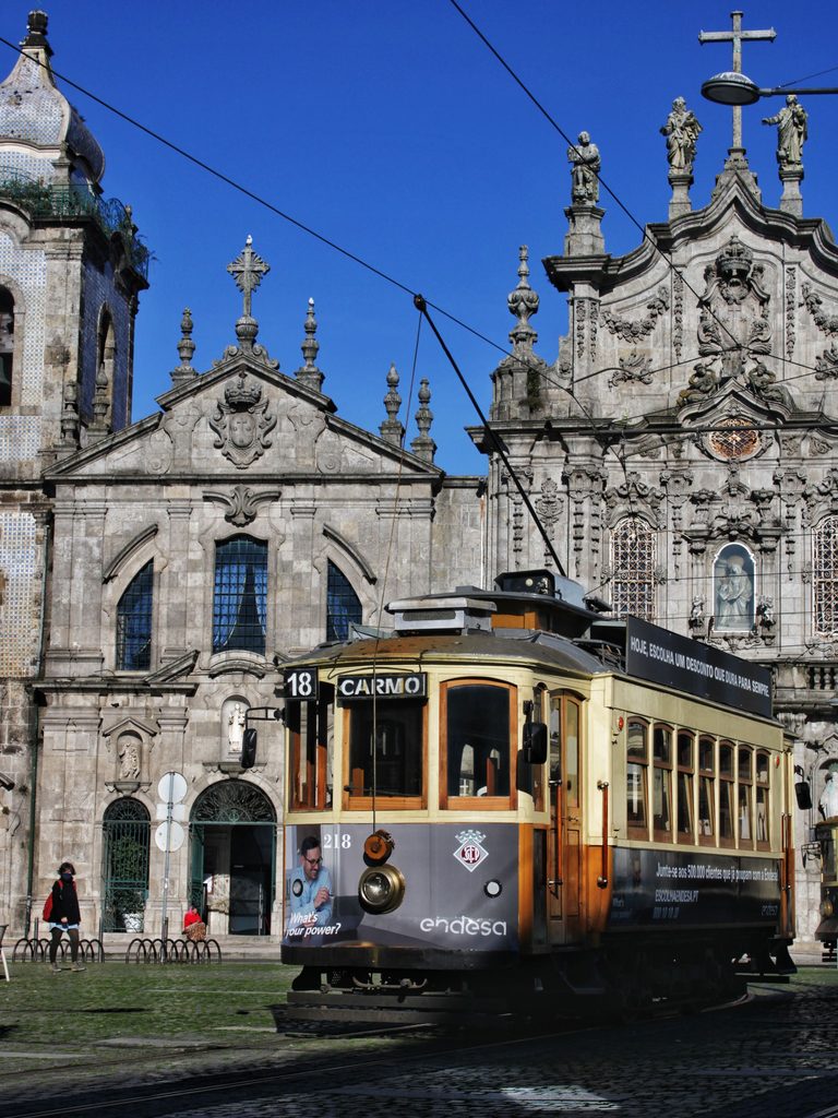 A vintage yellow and red tram passing in front of the twin churches of the Carmelitas and the Carmo in Porto