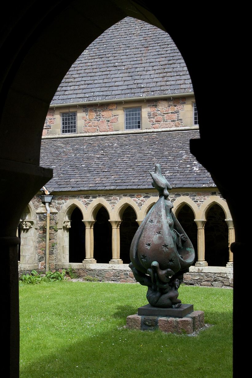 A bronze sculpture in the cloister garth of Iona Abbey seen through an arch