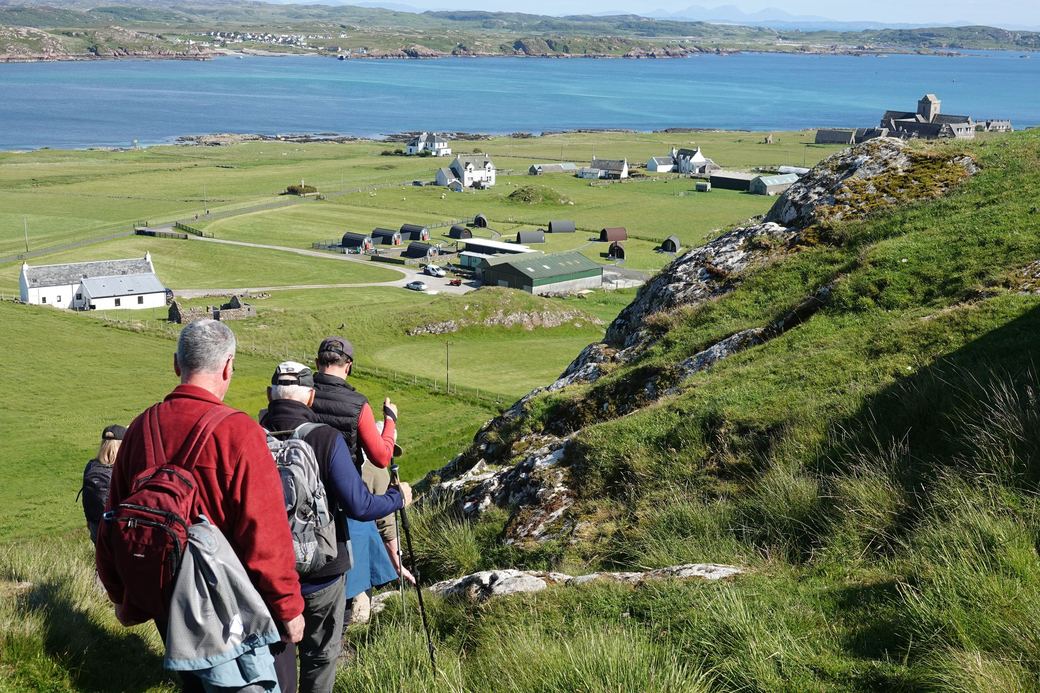 Walkers on a hillside above the village and abbey on Iona, with the Sound of Iona and Mull beyond