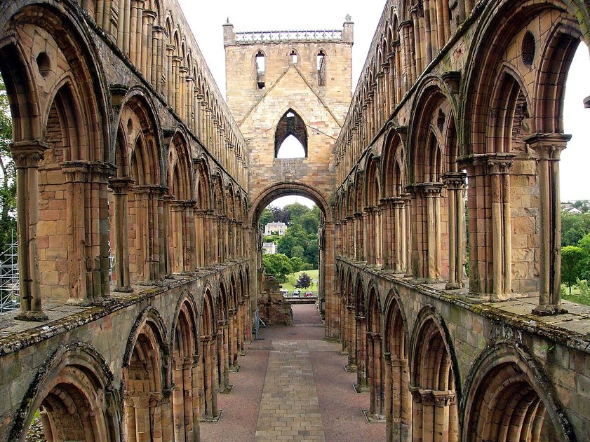 The roofless nave of Jedburgh Abbey, three tiers of arches on each side, looking west to the rose window