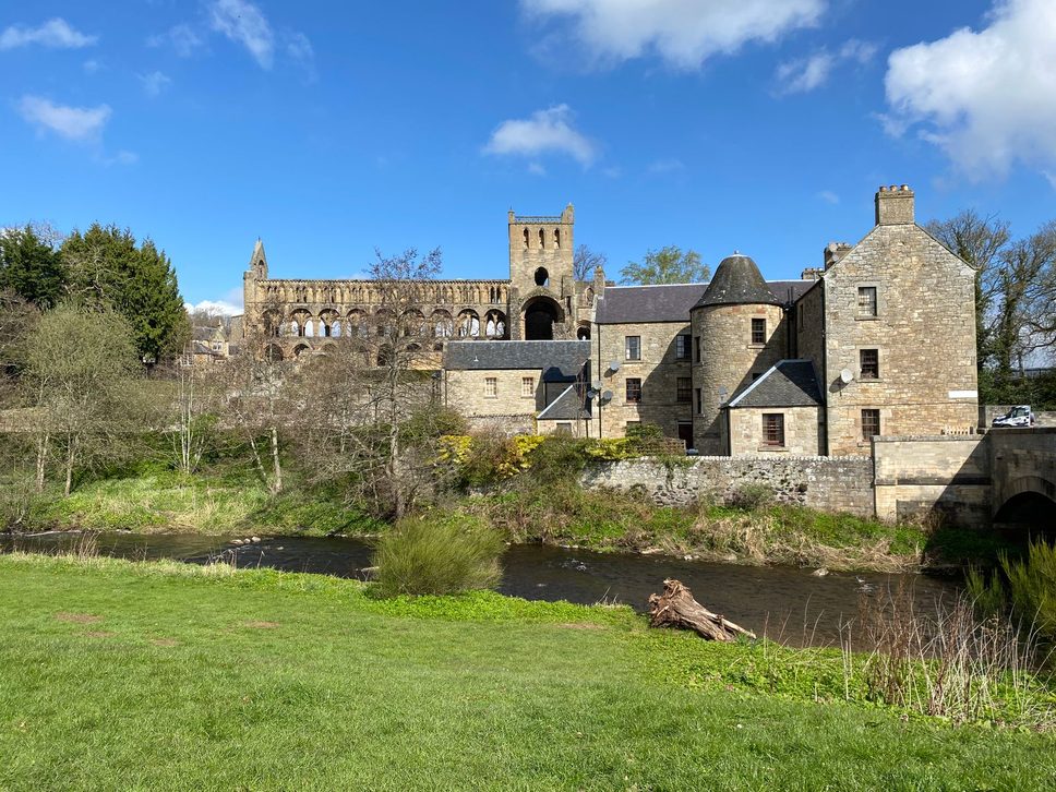 The ruined church of Jedburgh Abbey above the Jed Water, with its tower and long nave behind houses and the riverbank