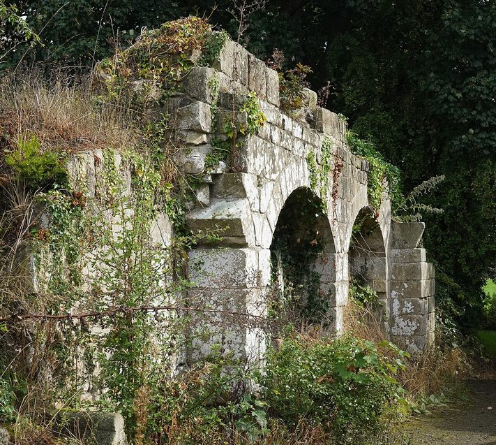 A row of ruined stone arches at Jervaulx Abbey overgrown with grasses and wild plants