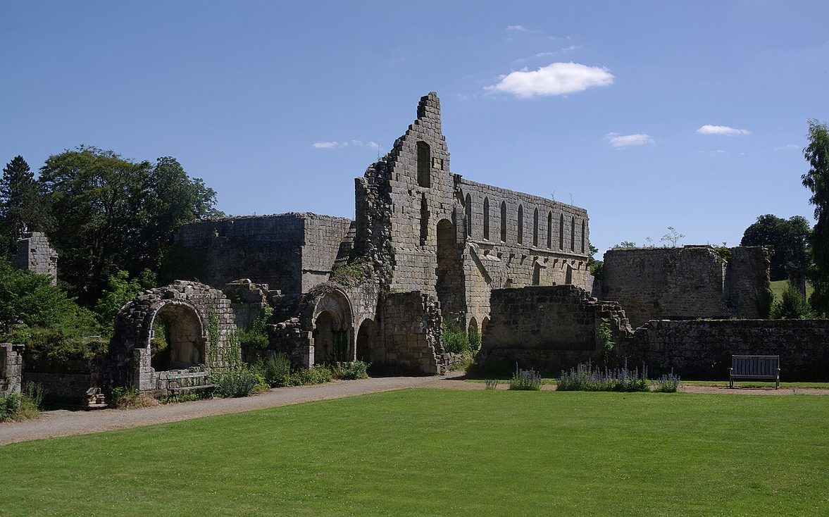 The ruins of Jervaulx Abbey, Wensleydale, with the tall wall of the monks' dormitory rising behind lawns and trees