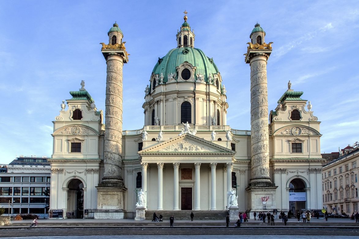The Karlskirche in Vienna, with its green copper dome between two tall carved columns, under a blue sky