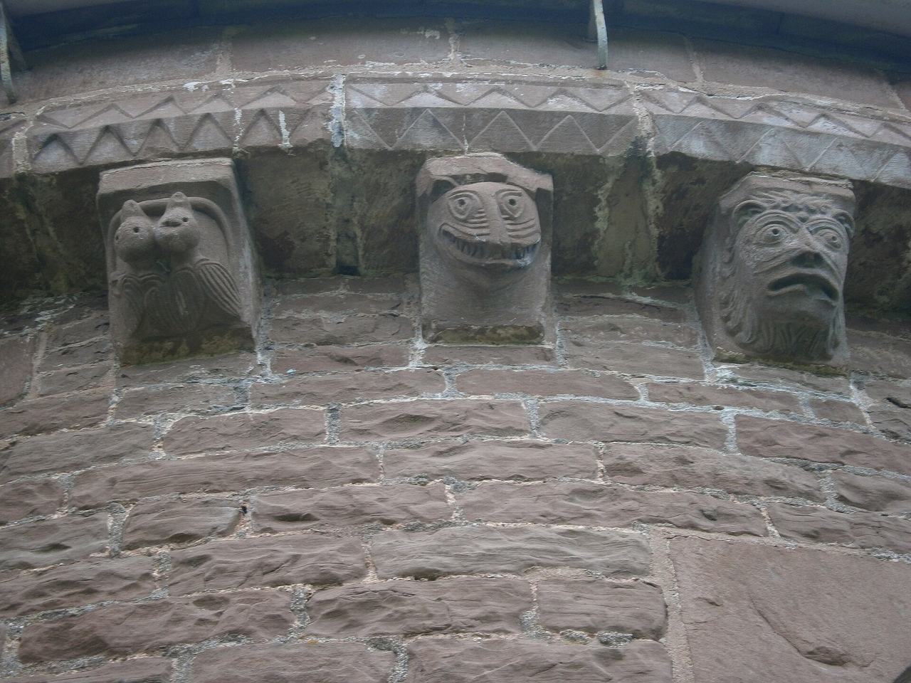 A row of carved stone corbels under the eaves of Kilpeck church, showing animal and human heads