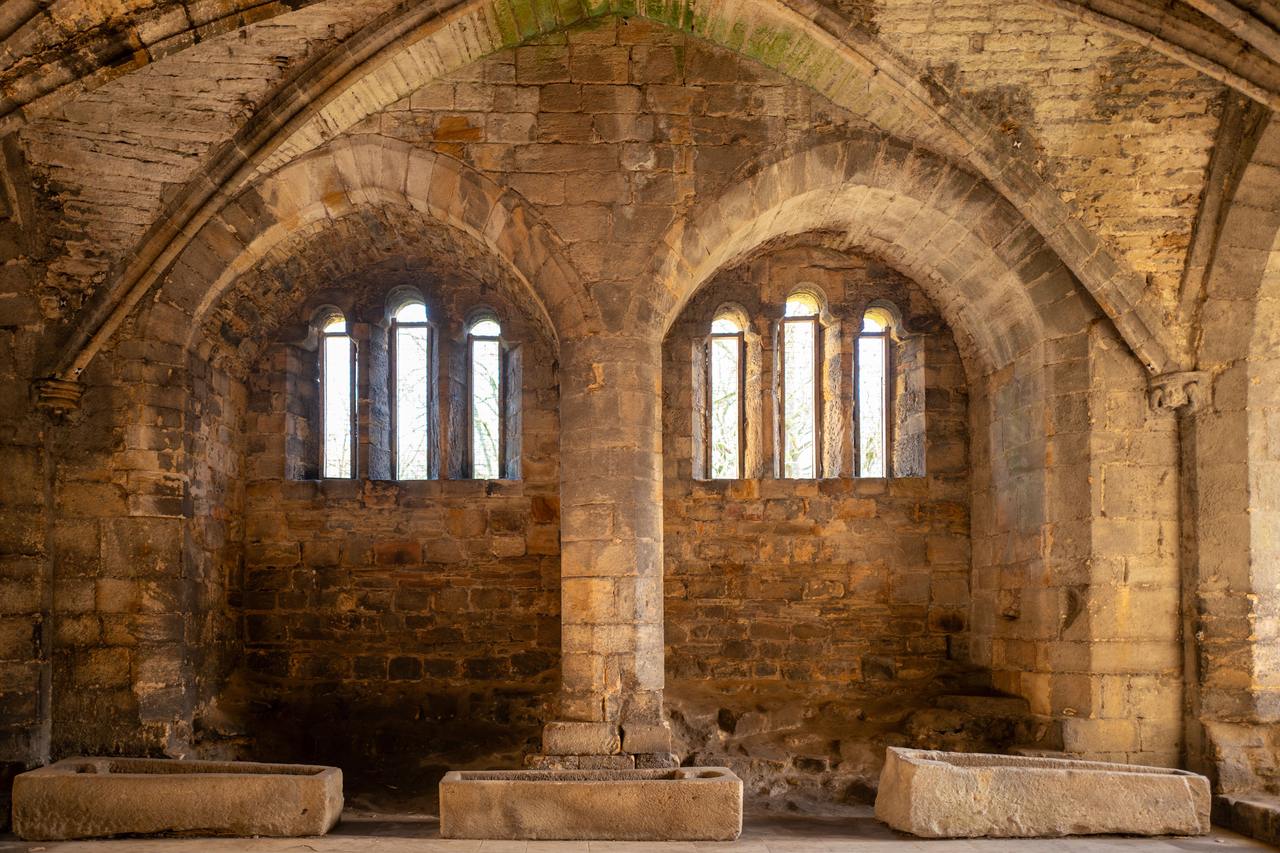 Round-headed arches and tall windows in the vaulted rooms of the east range at Kirkstall Abbey