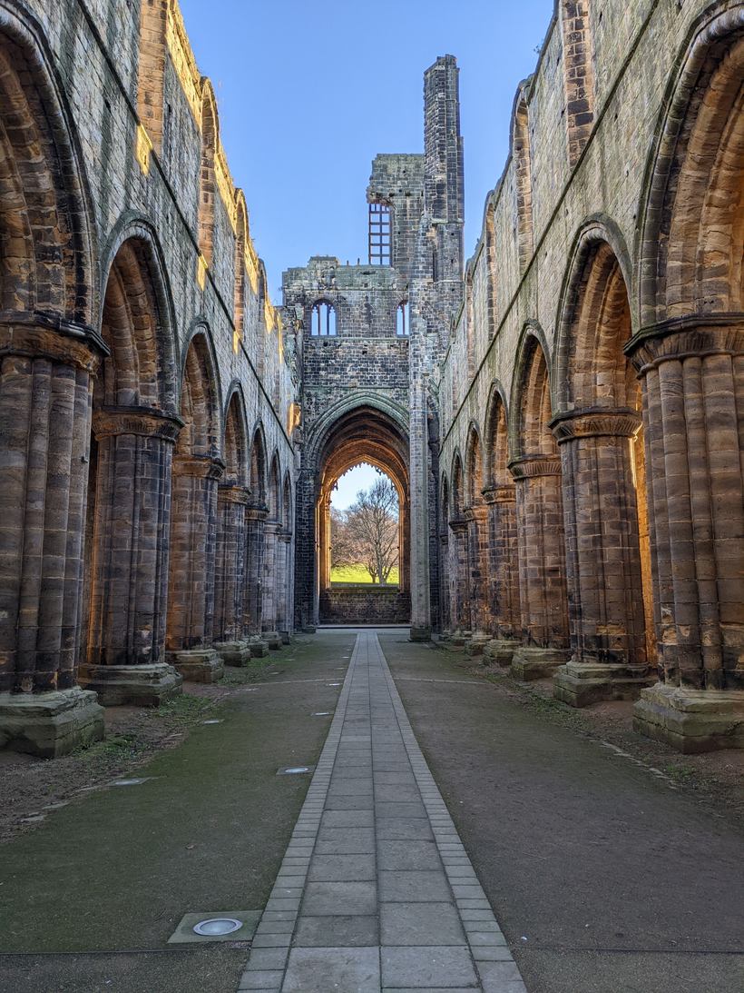 Looking along the nave of Kirkstall Abbey between rows of round pillars to the great west doorway