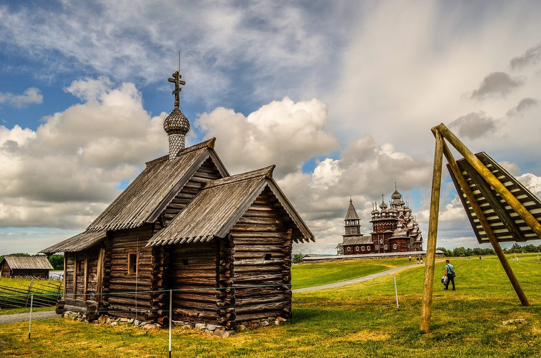 The small dark wooden Church of the Resurrection of Lazarus on Kizhi, with the domes of the Pogost in the distance