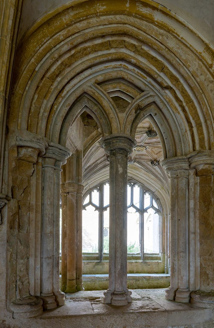 The vaulted medieval chapter house of Lacock Abbey, with plain stone walls and pillars