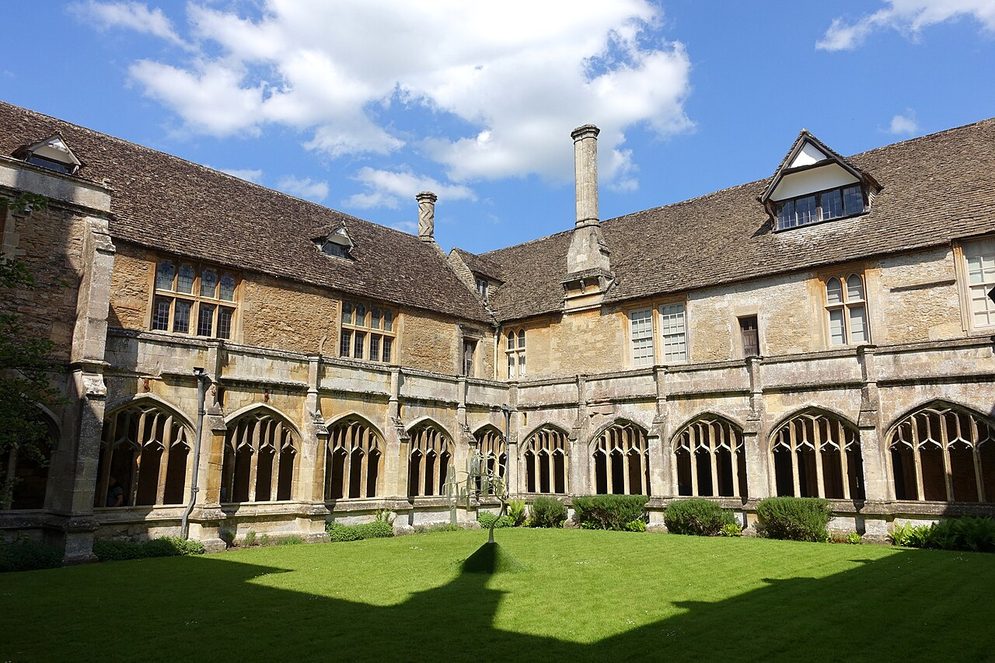 The cloister of Lacock Abbey seen across the grassed garth, with the house rising above