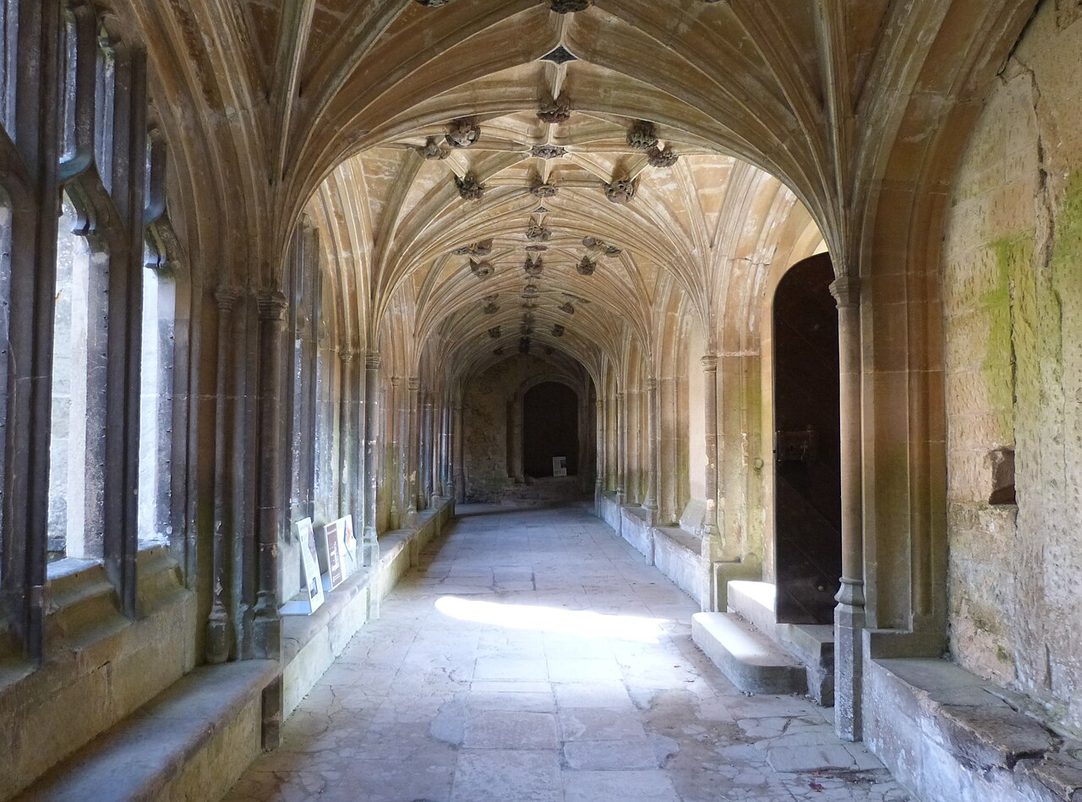 The vaulted medieval cloister walk of Lacock Abbey, with stone ribs and traceried openings onto the garth