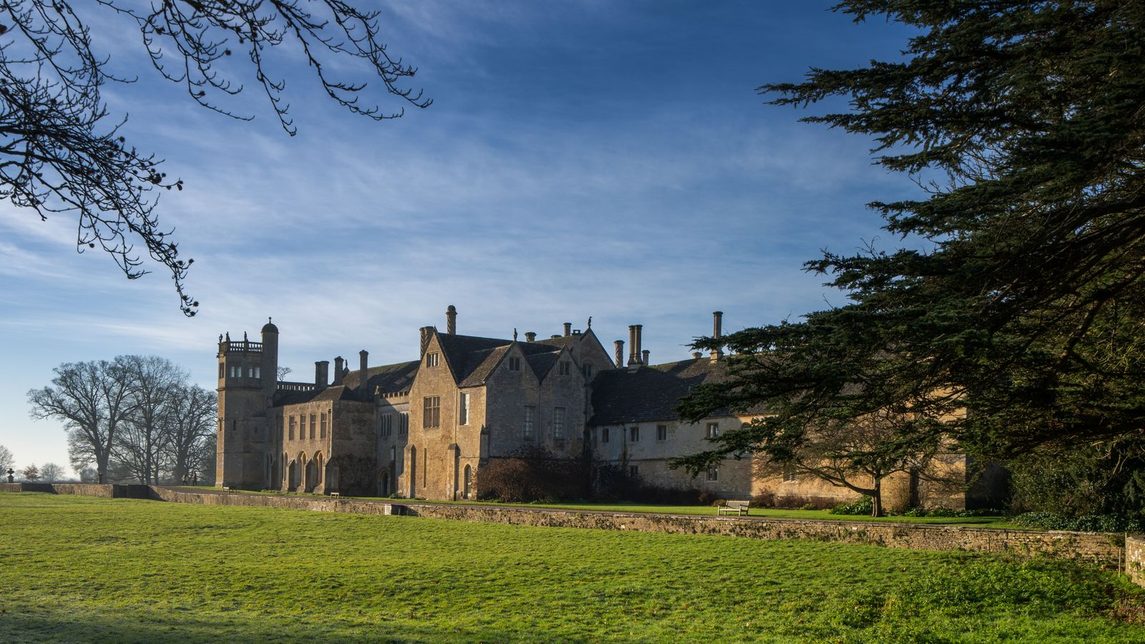 Lacock Abbey seen across its parkland, with trees and lawns in front of the house