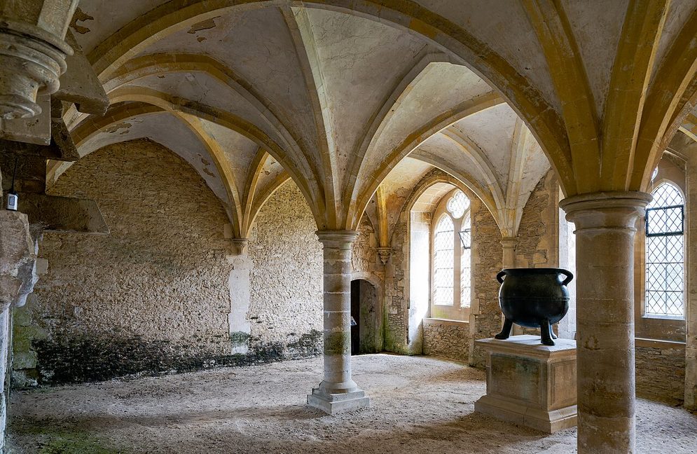 The vaulted warming house of Lacock Abbey, with a large stone fireplace and a big iron cauldron
