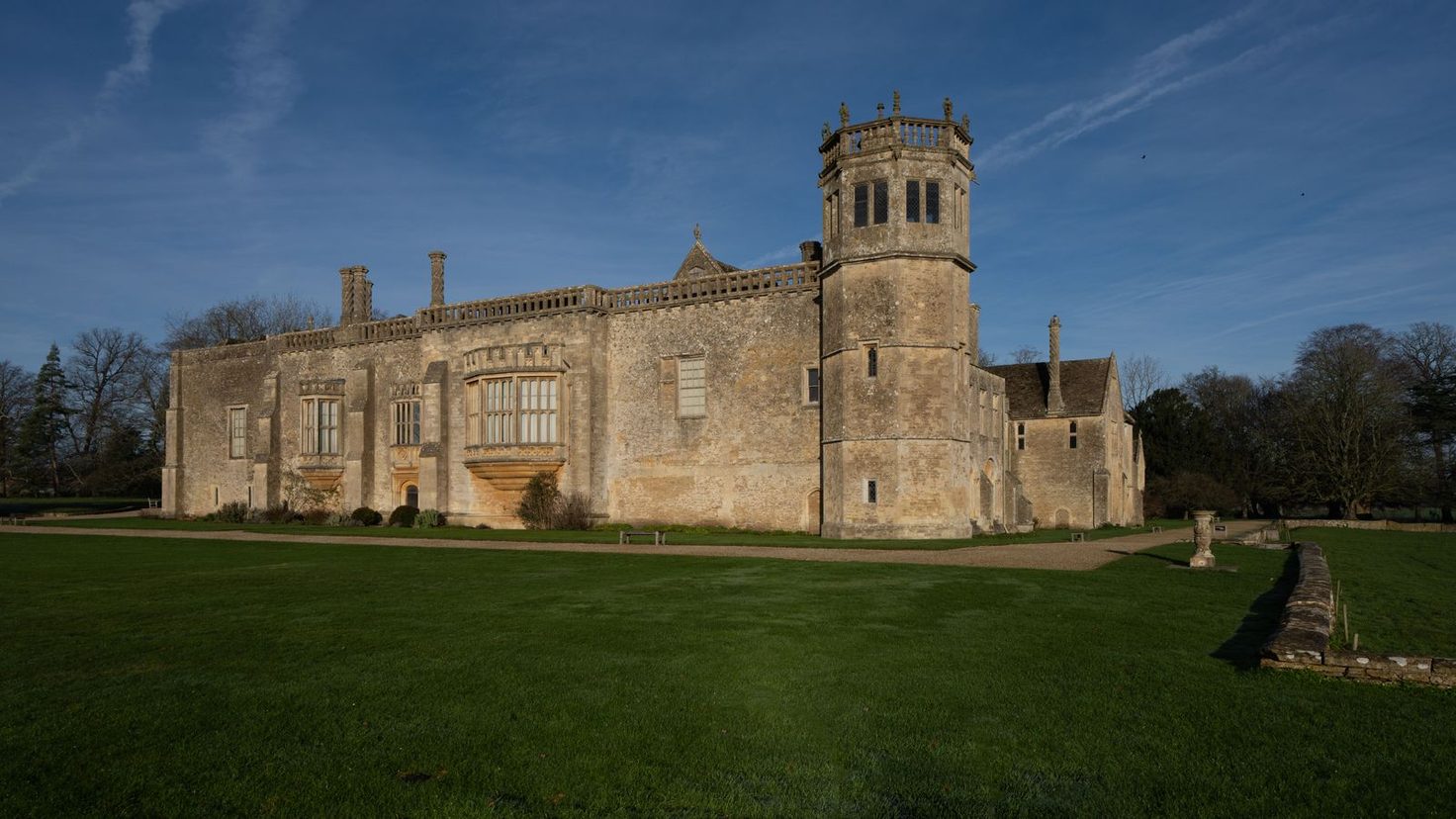 Lacock Abbey in Wiltshire, a long stone country house with an octagonal tower, seen across a lawn