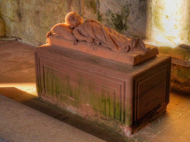 A carved effigy of a sleeping baby lying on a stone tomb chest at Lanercost Priory