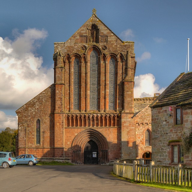 The tall west front of Lanercost Priory church with its lancet windows and a statue in a niche
