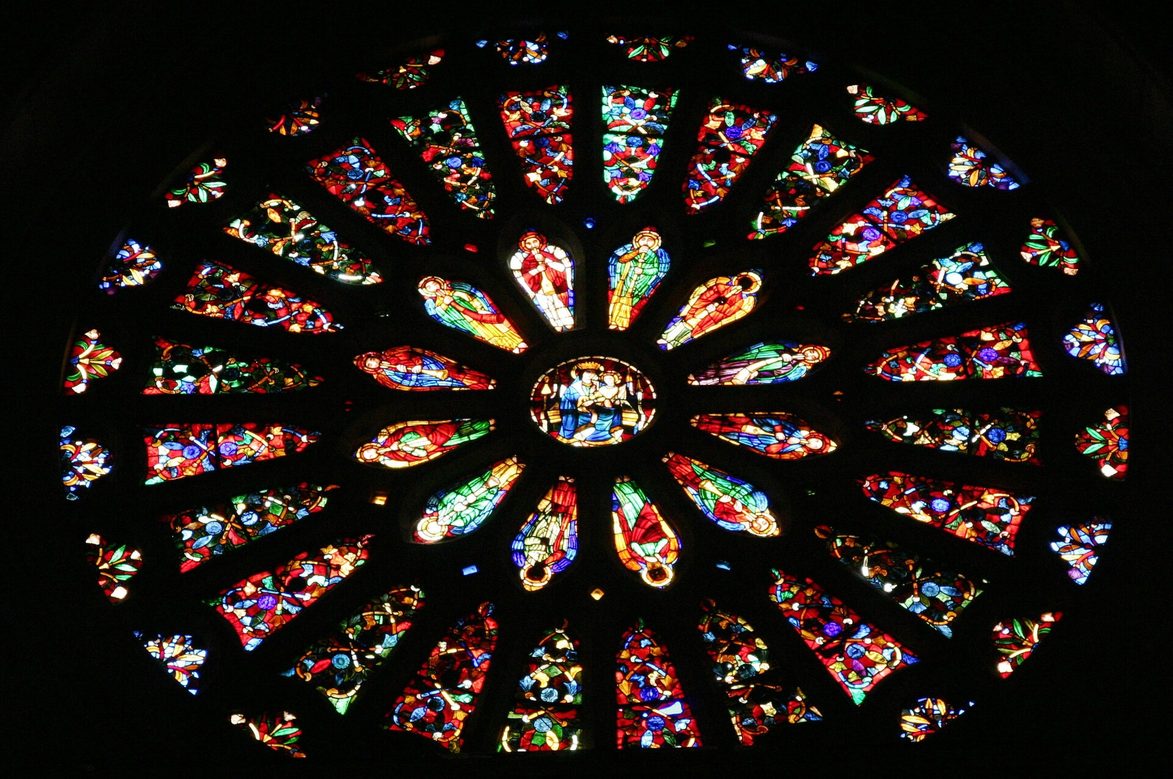 A Gothic rose window of León Cathedral seen from inside, glowing with coloured glass against the dark stone
