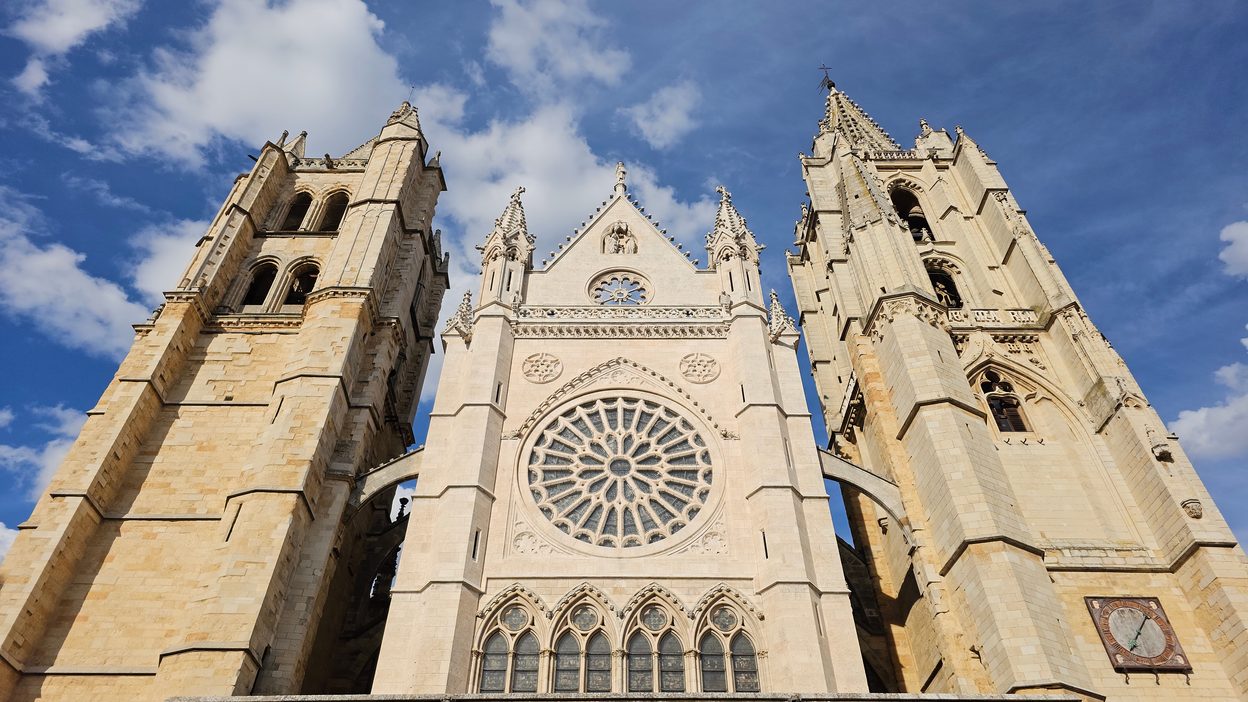 The Gothic west front of León Cathedral, with its rose window between two towers and a triple portal, on the Plaza de Regla