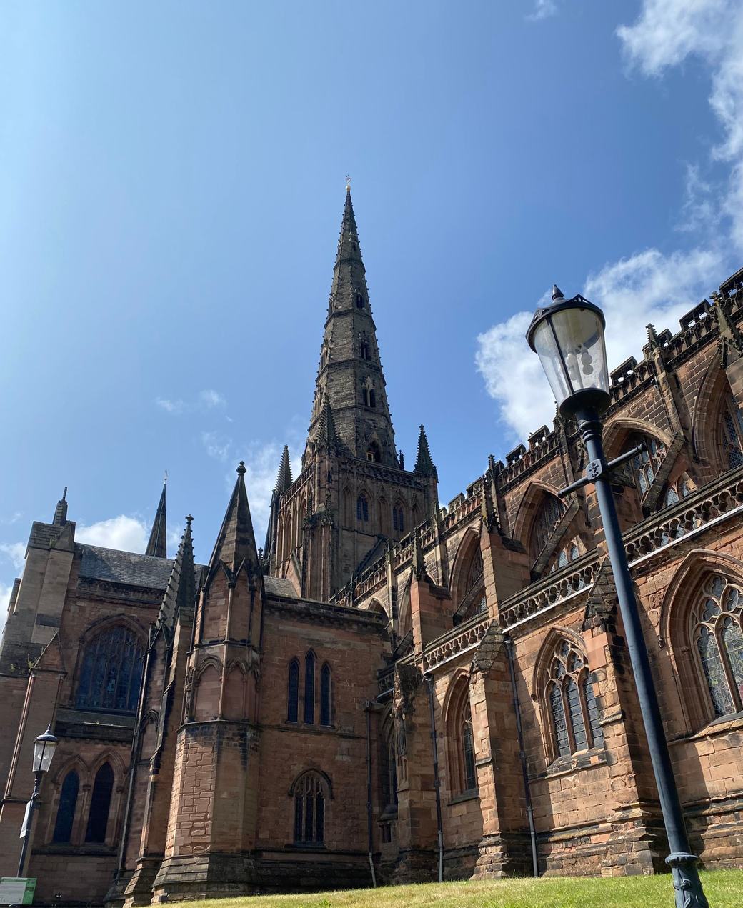 The red sandstone walls and central spire of Lichfield Cathedral against a blue sky