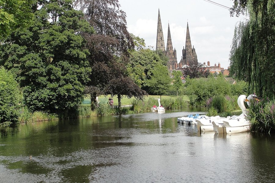 The three spires of Lichfield Cathedral seen over trees and Minster Pool