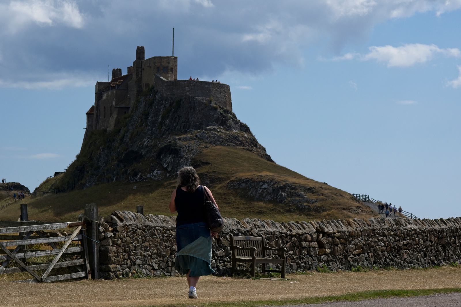 Lindisfarne Castle on its rocky crag above the shore of Holy Island, with a visitor walking towards it