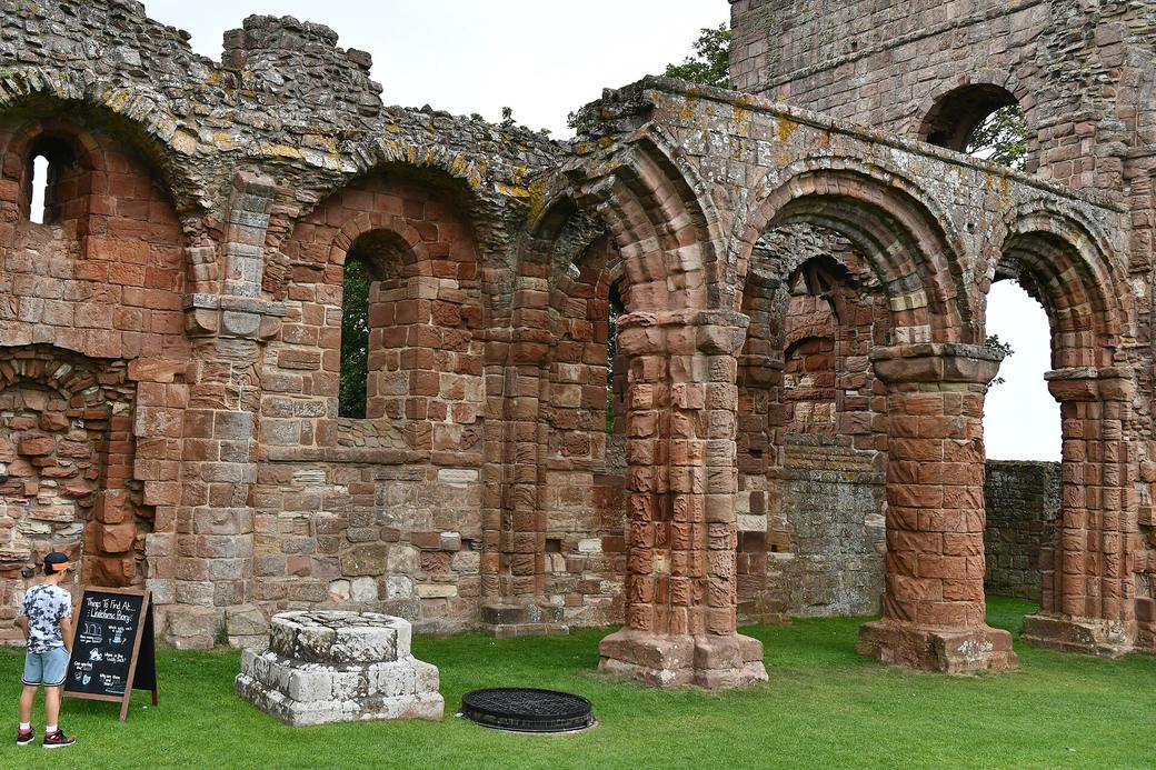 The ruined nave of Lindisfarne Priory with round Norman arches and a pillar carved with a chevron pattern