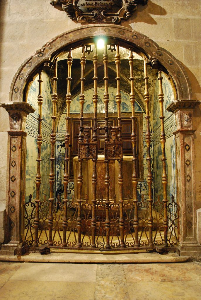 The baptismal font of Lisbon Cathedral behind an iron grille, in a chapel lined with blue and white tiles