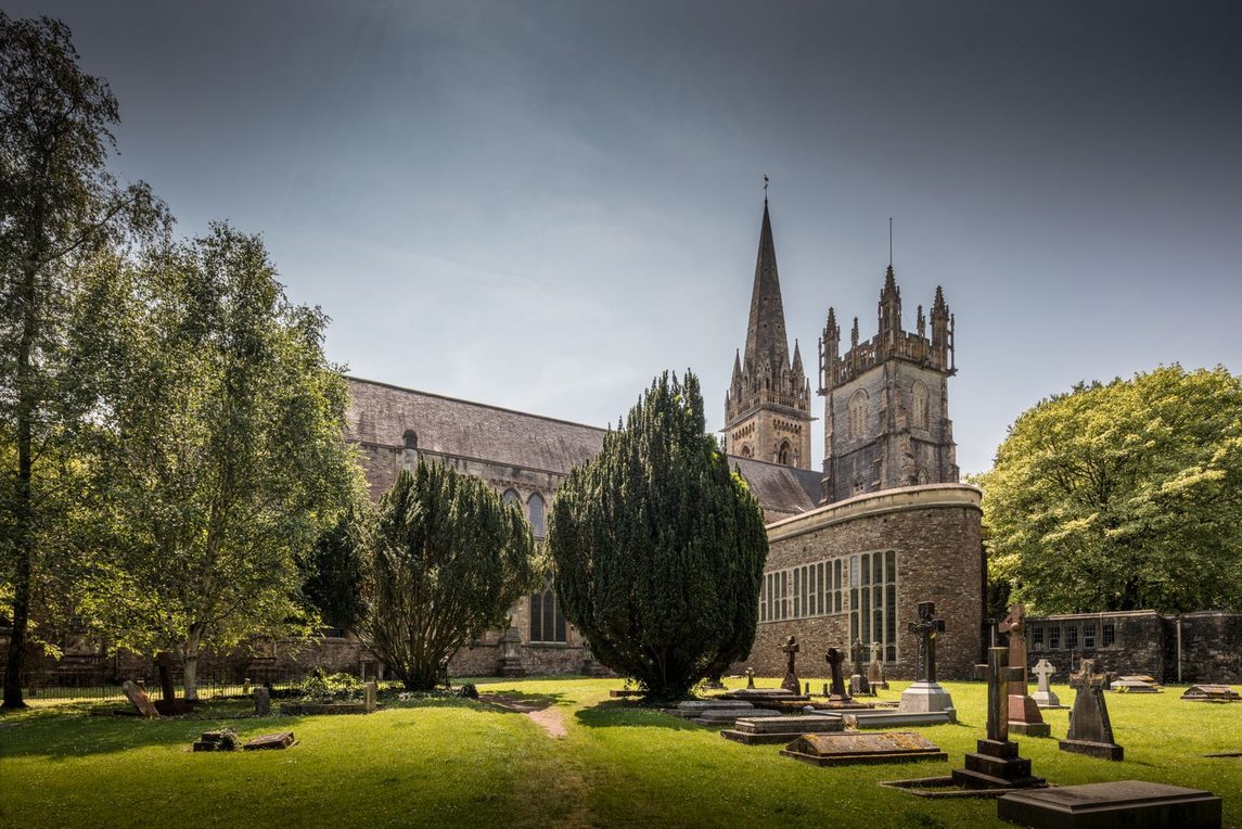Llandaff Cathedral, Cardiff, with its west towers and spire seen across the churchyard among trees