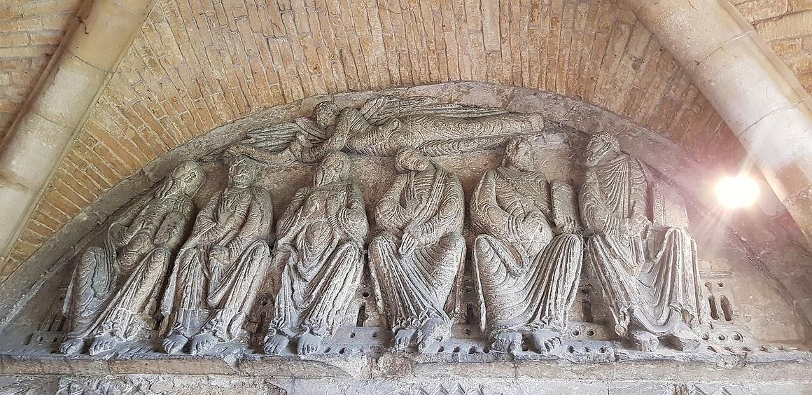 A carved stone panel of seated apostles beneath an angel, inside the porch of Malmesbury Abbey