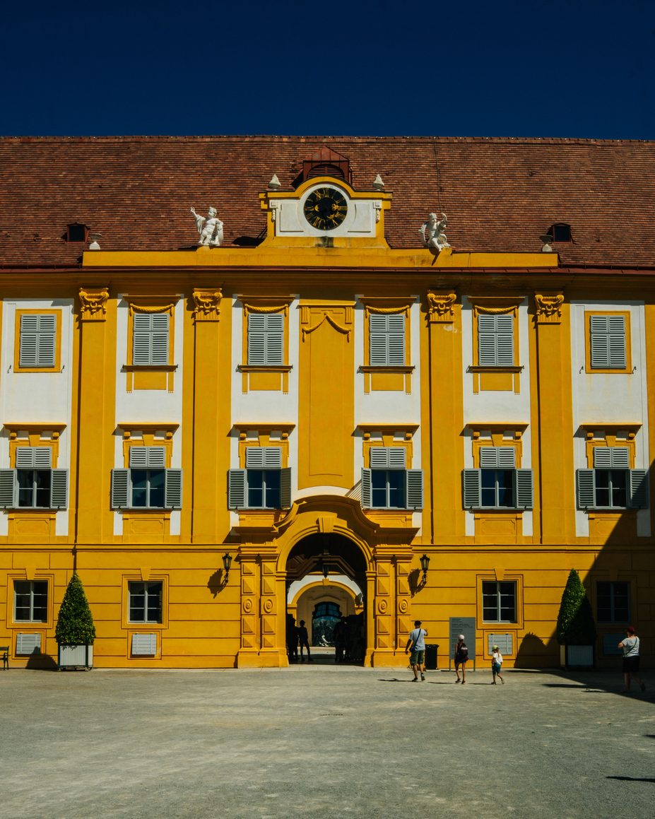The yellow facade and arched gateway of a forecourt building at Melk Abbey
