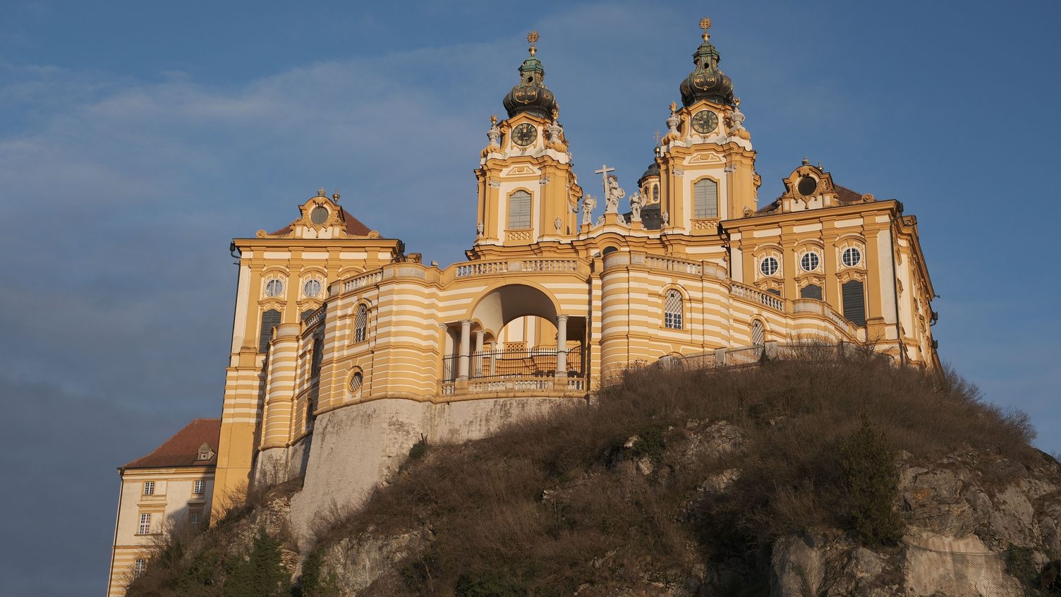 The yellow baroque church and buildings of Melk Abbey on their rock above the Danube, in evening light