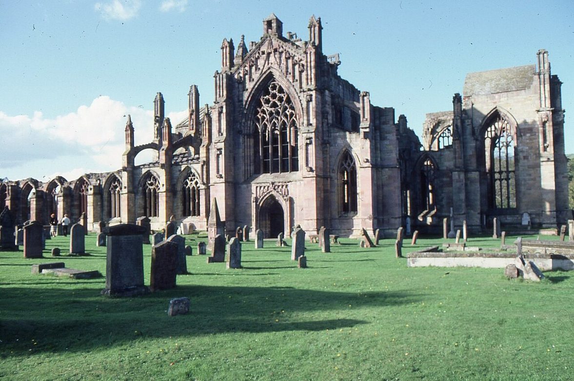 The ruined east end of Melrose Abbey with its tall Perpendicular east window, seen across the graveyard