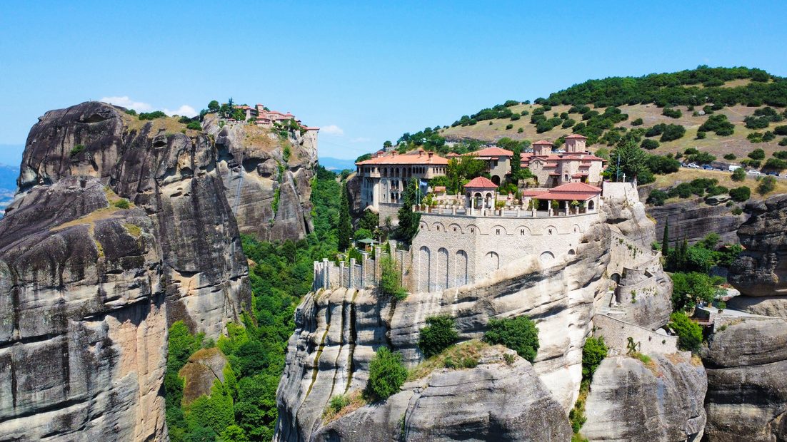 Monasteries built on top of towering sandstone pillars at Meteora, Greece, under a blue sky